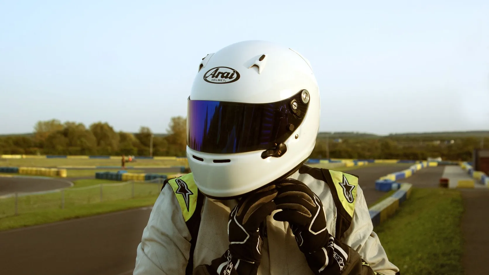 Karting driver fastening a full-face helmet beside an outdoor circuit