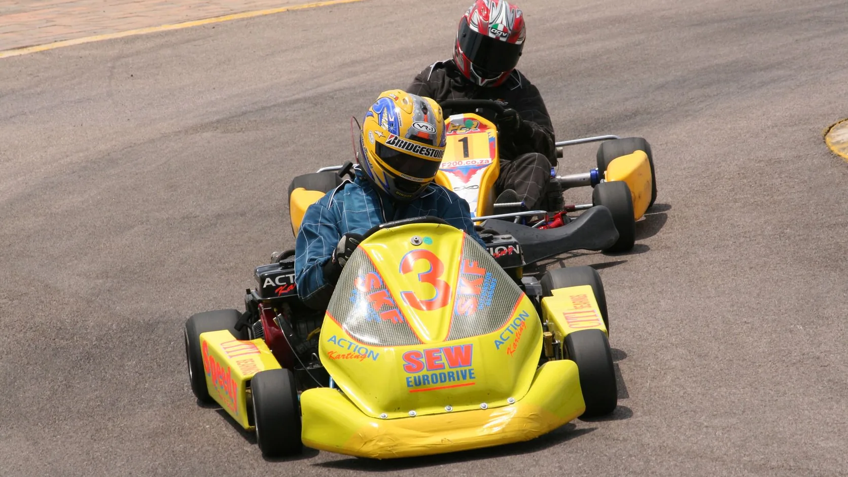 Two rental go-karts racing on an outdoor tarmac circuit